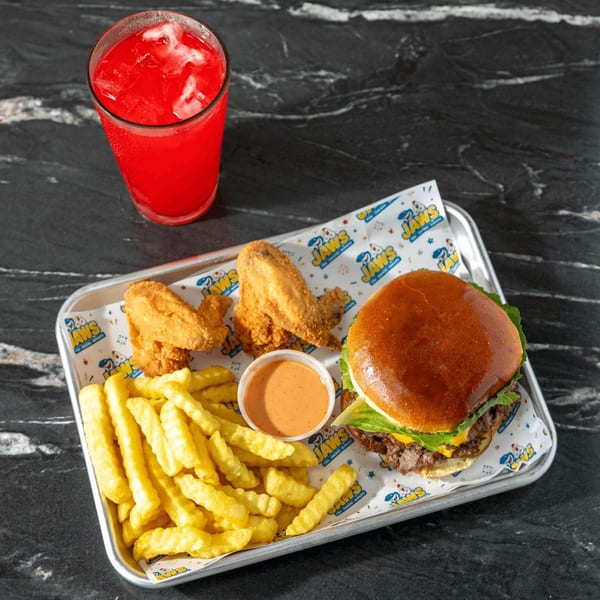 Burger with lettuce and cheese, crinkle-cut fries, fried chicken wings, dipping sauce, and red drink on a branded tray.