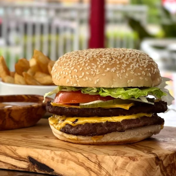 A double cheeseburger with lettuce, tomato, and pickles, served with potato wedges on a wooden board.