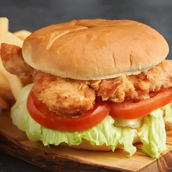 Crispy fried chicken sandwich with lettuce and tomato on a bun, served with fries.