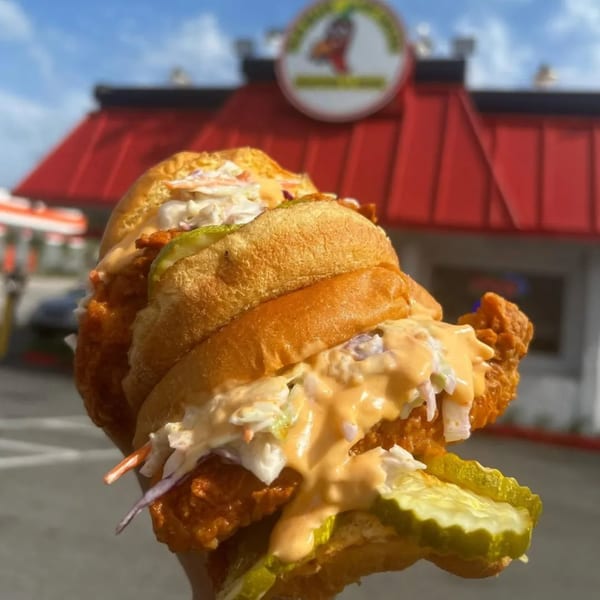 A Jaws Hot Chicken sandwich with coleslaw, pickles, and sauce, in front of the restaurant.