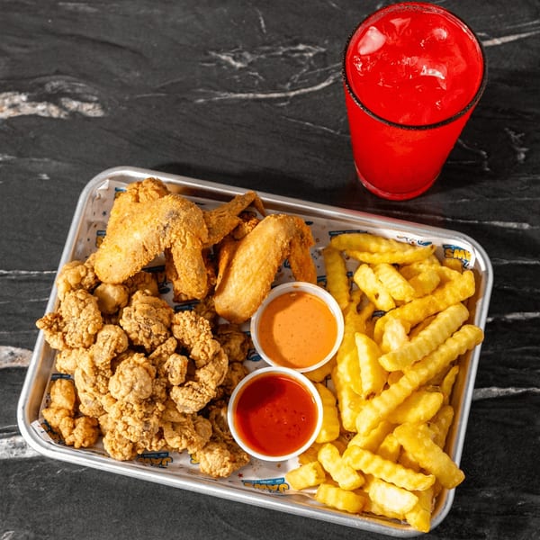 Tray of fried chicken, battered fish, fries, dipping sauces, and a red iced drink on a dark tabletop.