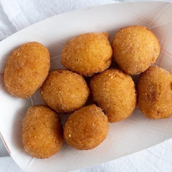 Eight golden-brown hush puppies, a classic American side dish, served in a white paper tray.