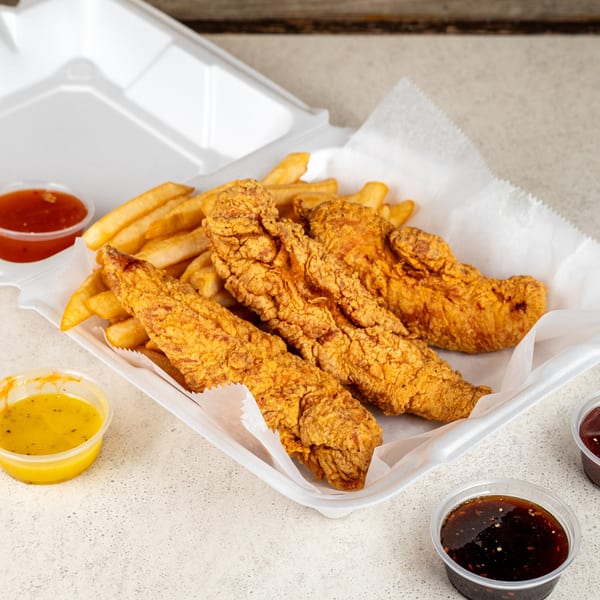 Crispy fried chicken tenders and french fries in a white takeout container with dipping sauces.
