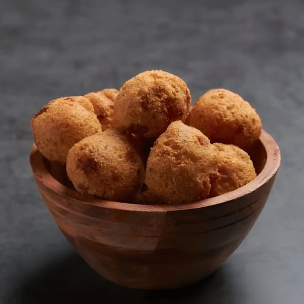 A wooden bowl filled with golden-brown, breaded hush puppies, against a dark background.